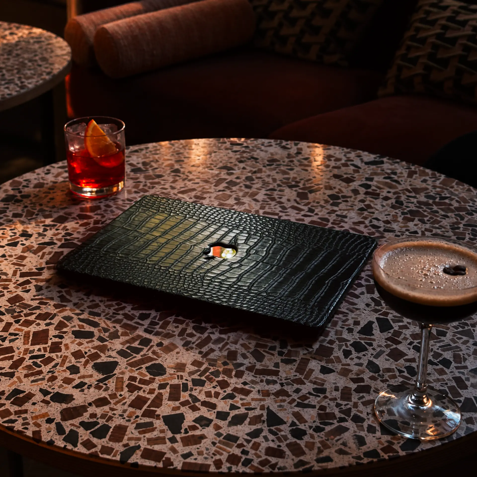 Green crocodile-embossed leather MacLeather case on a terrazzo café table with cocktails