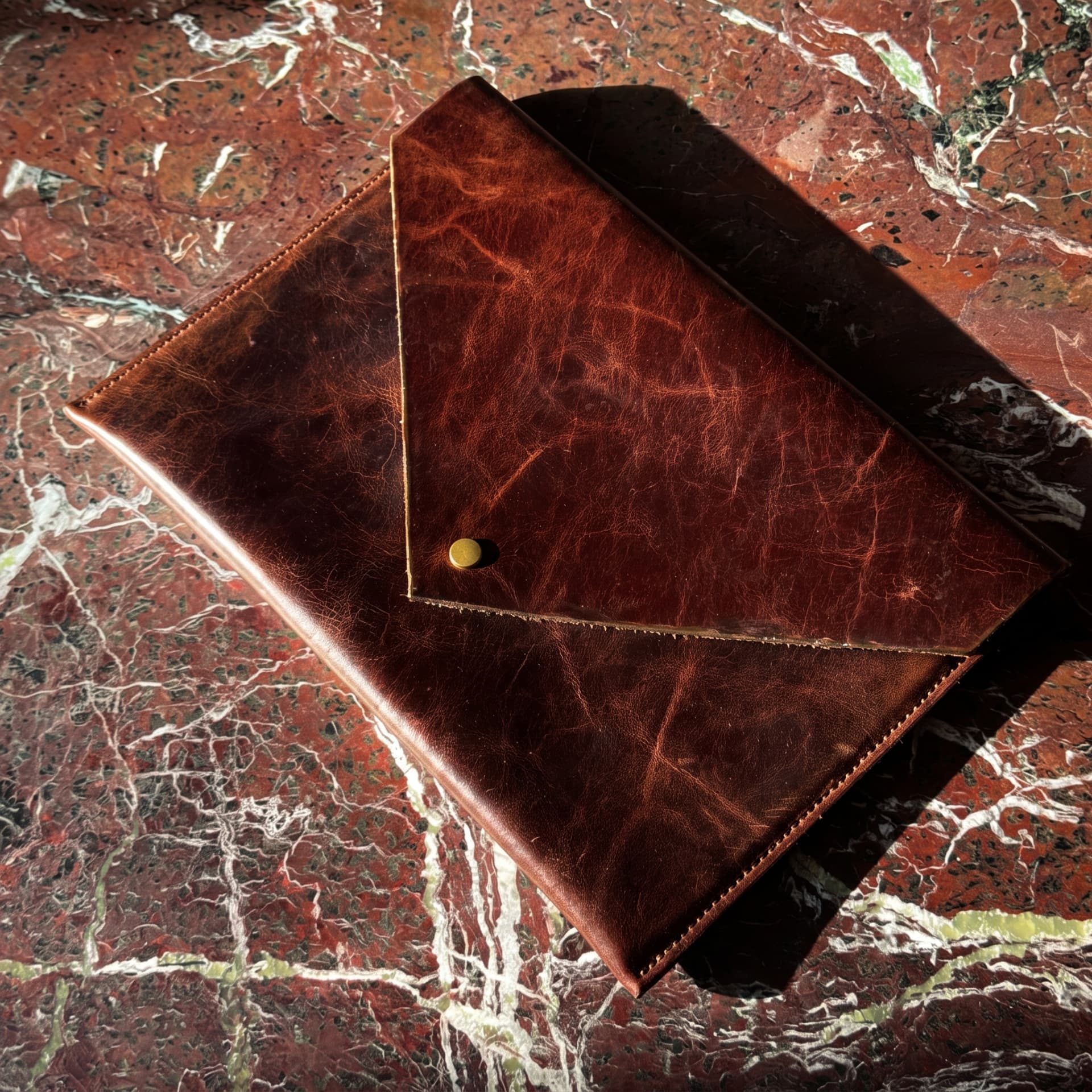 Brown leather MacLeather envelope with a brass snap on red marble