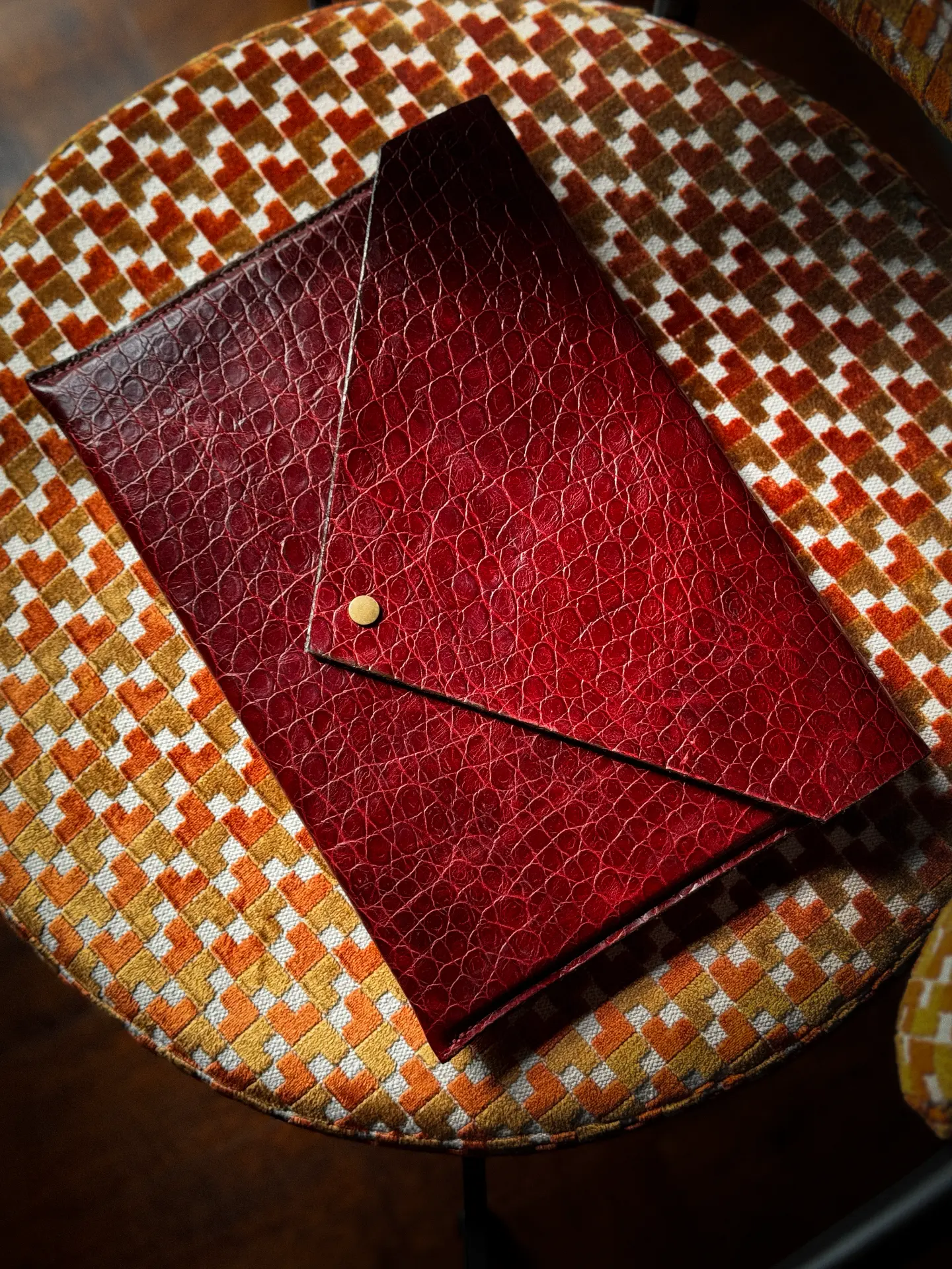 Two red leather MacLeather envelopes on a patterned velvet chair